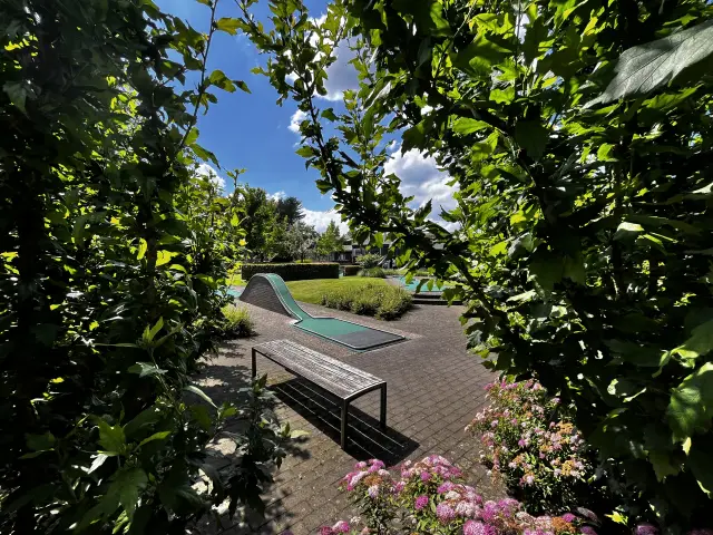 Tuinpad met minigolfbaan omgeven door groene hagen en bloemen