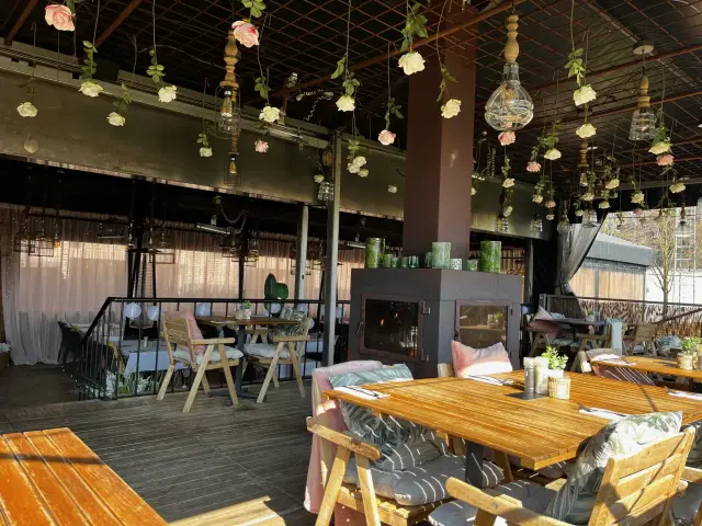 Overdekt terras met houten tafels, kussens en hangende rozen aan het plafond