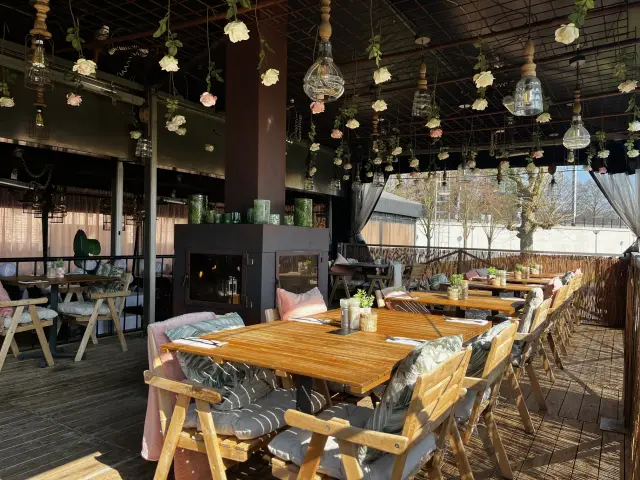 Overdekt terras met houten tafels, sfeerhaard en bloemendecoratie aan plafond