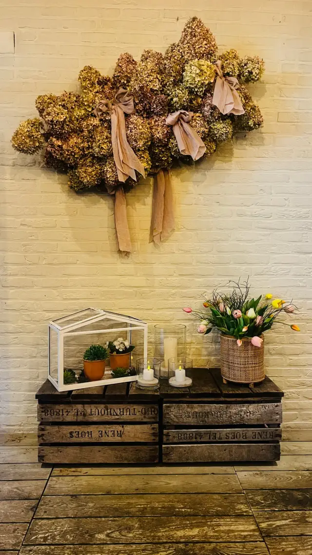 Decoratieve hoek met gedroogde bloemen aan de muur en houten kratten met plantjes en kaarsen