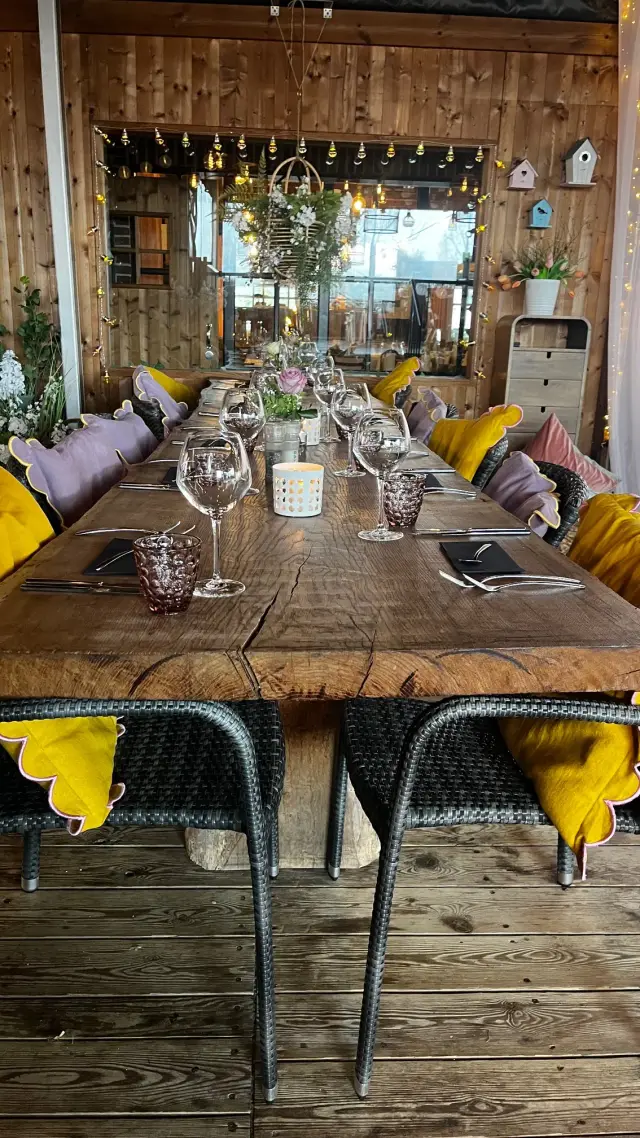 Lange gedekte tafel met wijnglazen, kaars en gele servetten in houten eetruimte