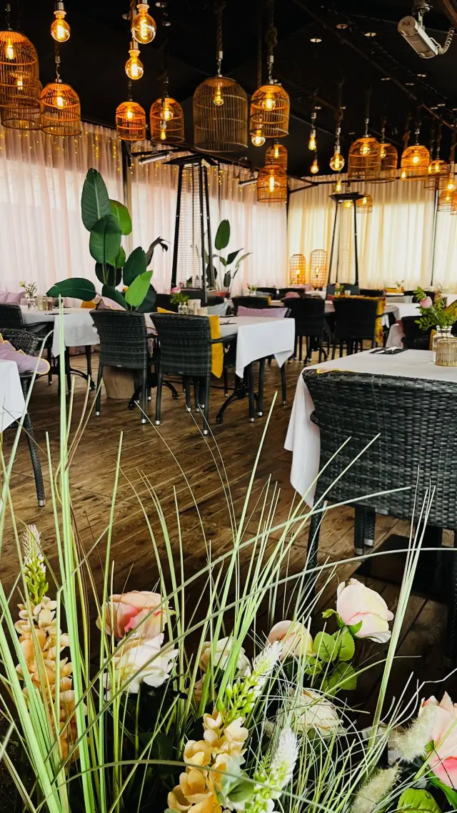Eetzaal met gedekte tafels, rotan stoelen en sfeerverlichting in vogelkooivorm