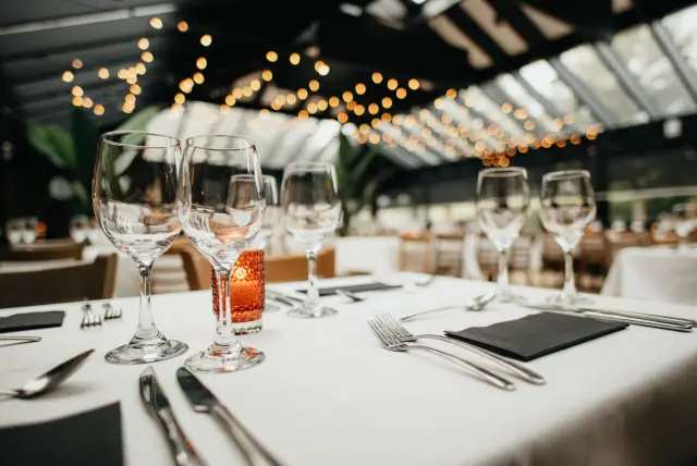 Gedekte tafel met wijnglazen en bestek in feestzaal met lichtjes aan het plafond