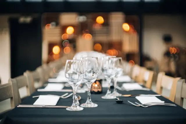 Lange gedekte tafel met wijnglazen en donkere tafellinnen in feestzaal met lichtjes