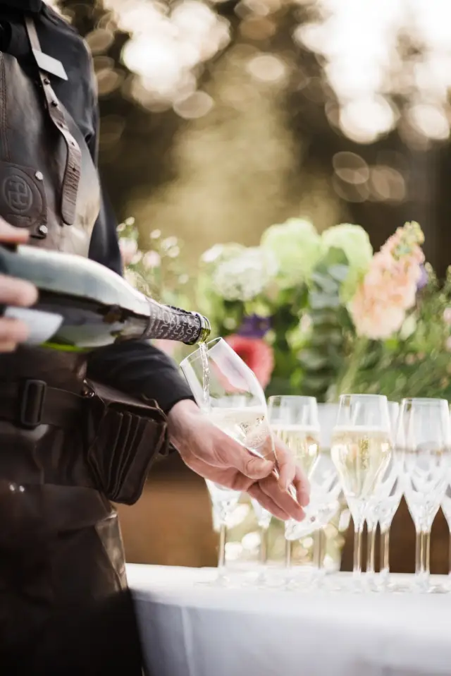 Ober schenkt champagne in glazen bij een tafel met bloemen buiten