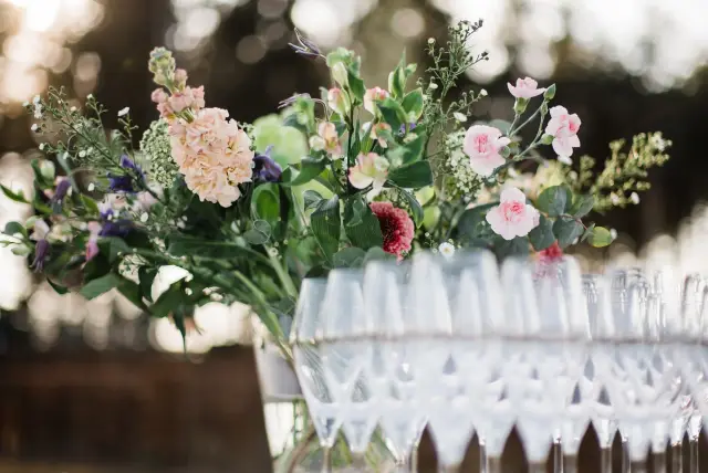Bloemstuk met roze, perzik en paarse bloemen bij glazen op tafel, buiten in tegenlicht
