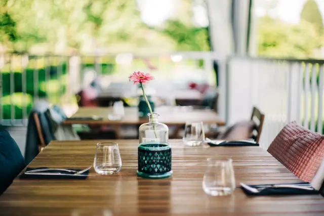 Gedekte tafel op terras met glazen en bloem in vaasje, wazig uitzicht op groen op achtergrond
